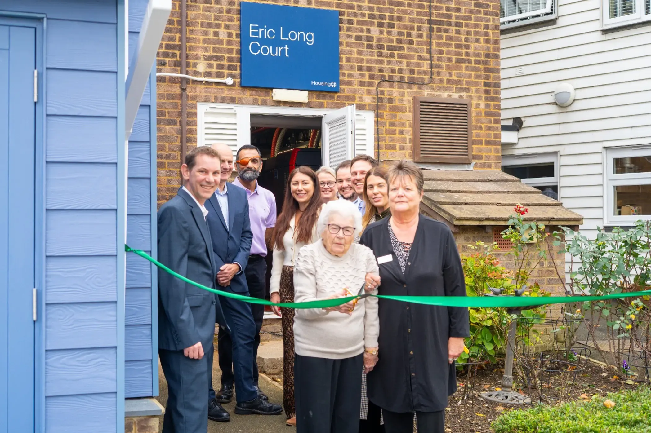 Elderly resident cutting the ribbon celebrating the official switching on of the newly installed renewable heating and energy system.